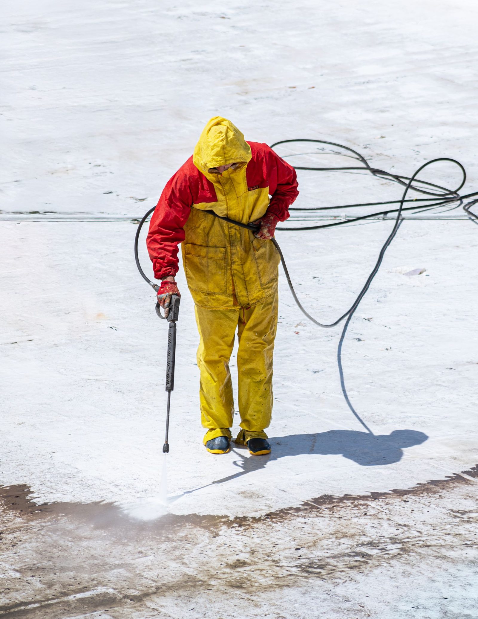 Worker in protective overalls pressure washing a concrete surface